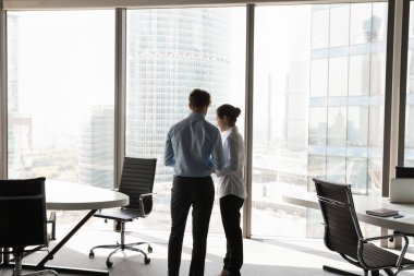 Çağdaş ofis içinde konuşan iki genç iş arkadaşı panoramik pencere camı duvarında iş projesini tartışıyorlar. İşbirliği, müzakere, iş konsepti