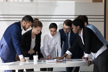 Çok ırklı bir iş grubu proje stratejisi, planı tartışıyor, toplantı masasında duruyor, kağıt raporlarını analiz ediyor, problem çözme üzerine beyin fırtınası yapıyor. Takım çalışması konsepti