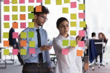 Çeşitli milenyum çalışanları, proje programını tartışan iş arkadaşları, yapışkan notlar yazan notlar. Başlangıç lideri, koç, genç stajyer çocuk eğitmeni, Kanban yönetim kurulunu görev planlama için kullanıyor.