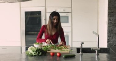 Dertsiz, güzel Hintli kadın ev mutfağında yemek pişiriyor ve dans ediyor, salata için sebze kesiyor, organik beslenmenin tadını çıkarıyor, sağlıklı yaşam tarzı, lezzetli yemekler, müzik, hareket