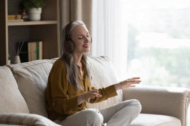 Huzurlu yaşlı kadın kaliteli sesten hoşlanır, evdeki kanepede tek başına oturan kablosuz kulaklıklarla en sevdiği şarkı. Dijital müzik hizmetleri kullanıcısı, modern teknoloji, ruh konsepti için boş zaman aktivitesi