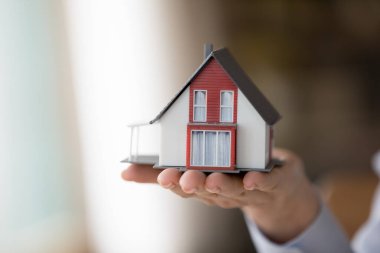 Avuç içi kadar küçük bir evde el ele tutuşan bir kadın. Gayrimenkul alımı, yeni mülk satışı, inşaat şirketi müşteriye kârlı ticari teklifler, mülkiyet, banka kredisi kavramı