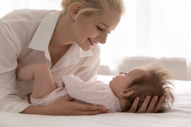 Yakın çekim, sevgili anne yeni doğmuş güzel kızına dokunur. Vücut giysisi giymiş bebek kızı evde ya da doğum hastanesinde rahat bir yatakta birlikte yatar. Mutlu annelik, aşk, aile bağları konsepti