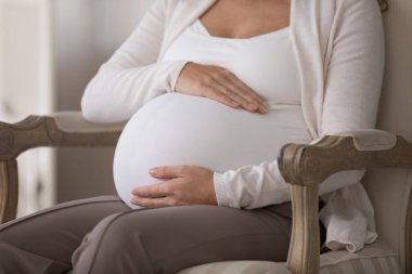 Geç hamilelik, hamilelik, tüp bebek prosedürü konsepti. Kesilmiş yakın çekim kimliği belirsiz hamile kadın karnına dokunuyor, hamile anne üç aylık hamile karnına avuç içlerini koltuğa koyuyor.