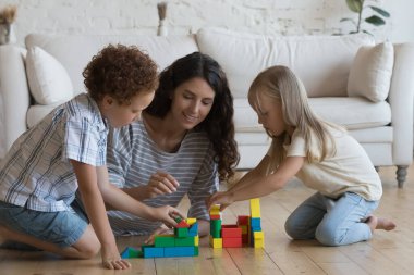 Mutlu 30 'lu yaşlardaki anne ve iki odaklı anaokulu çocuğu birlikte ısıtma katında oynuyorlar, kuleler inşa ediyorlar, renkli bloklardan oyuncak şato yapıyorlar, aile yaratıcılığının tadını çıkarıyorlar, ev aktiviteleri yapıyorlar.