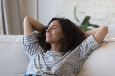 Huzurlu, güzel Latin bir kadın evdeki kanepede dinleniyor, arkasını yaslıyor, serin havayı soluyor, sakinliğin tadını çıkarıyor, dinleniyor, hafta sonu, dinleniyor, meditasyon yapıyor, stres atağı yapıyor.