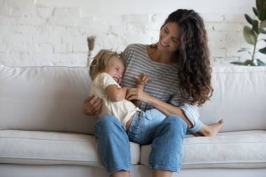 Neşeli, mutlu bir anne, heyecanlı bir kızı gıdıklıyor, kucağında çocuk, sarılıyor, sarılıyor, eğleniyor, anneliğin tadını çıkarıyor, çocuk bakıcılığı yapıyor, aile kanepesinde boş vakitlerini geçiriyor.