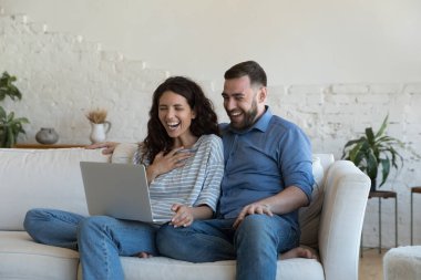 Neşeli evli çift başarıyı kutluyor, kazanıyor, laptopta kar ediyor, bakıyor, ekrana bakıyor, şaşkınlık içinde gülüyor, sürpriz yapıyor, video çağrısından harika haberler alıyor.