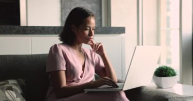 Düşünceli serbest girişimci kadın bakışlarını kaçırıyor, düşünüyor, ilham arıyor, aha parmak hareketi yapıyor, dizüstü bilgisayara dönüyor, daktilo yazıyor, ev kanepeden online iş projesi üzerinde çalışıyor.