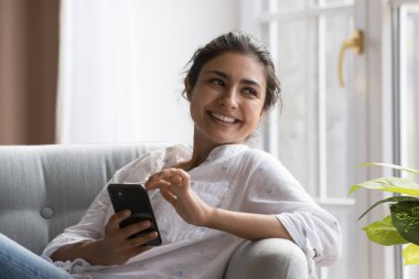 Huzurlu Hintli kadın rahat koltukta akıllı telefonuyla rahatlıyor, yan yana bakıp gülümsüyor tasasız hafta sonunun ve modern kablosuz teknolojinin tadını çıkarıyor. Arama yapmak, mal ve hizmetleri online sipariş etmek, e-randevu uygulamaları kullanmak