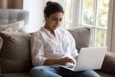 Evde dizüstü bilgisayar kullanan, internetten çalışan çekici odaklı Hintli kadın ciddi görünüyor, elektronik ticaret sitesinden sipariş veriyor. Modern kablosuz teknoloji kullanımı, mesafeli iletişim