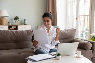 Mutlu 30 'lu yaşlardaki Hintli kadın kağıt mektupta iyi haberler okuyor, kredi onayıyla ilgili banka tebligatını okuyor, işi, eğitimi veya kişisel başarıyı kutluyor, zevk başarısı, yeni iş fırsatı, vergi iadesi