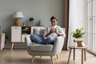 Güzel Hintli bir kadın şık, rahat bir oturma odasında koltukta dinleniyor. Akıllı telefon kullanıyor, internette sohbet ediyor, elektronik servisler vasıtasıyla telefon ediyor ya da sipariş veriyor. Eğlence ve iletişim için modern teknoloji kullanımı