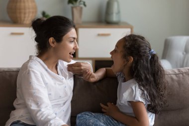 Genç Hintli anne ve tatlı kız birlikte konuşma alıştırması yapıyorlar, evdeki koltukta ses egzersizleri yapıyorlar, terapist logopedisi anaokulu kızının telaffuzunu düzeltiyor, kekeme çocuğa yardım ediyor.