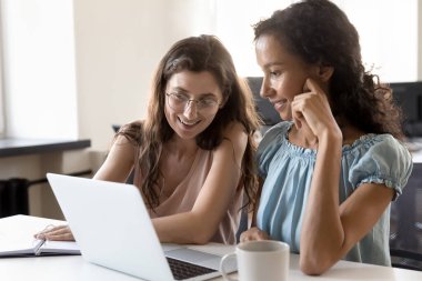 Birlikte dizüstü bilgisayar kullanan iki mutlu ofis arkadaşı, görevler için bilgisayarı paylaşıyor, proje üzerinde işbirliği yapıyor, iletişim kuruyor, görüntüye bakıyor, gülümsüyor, gülüyor.