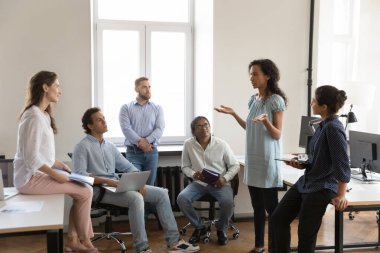 Serious African American business team employee making report to colleague on office meeting. Project leader speaking before group. Company teacher training new workers, explaining tasks