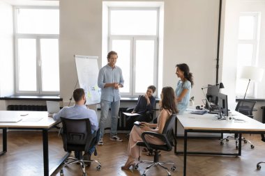 Mutlu çoklu etnik çalışanlar beyin fırtınası yapıyor, ofis alanında gülüyor, kiralık çalışma alanında buluşuyor, daireler çiziyor, gülüyor, takım liderinin pazarlama raporunu dinliyor, takım çalışmasından keyif alıyor.