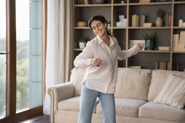 Heyecanlı, aktif, kablosuz kulaklığı olan, müzik dinleyen, müzik listesinden ezgiler çalan, favori şarkılar, oturma odasında dans eden, gülümseyen, gülen bir İspanyol kız. Mutlu kadın eğlenceli ev aktivitelerinden hoşlanıyor.