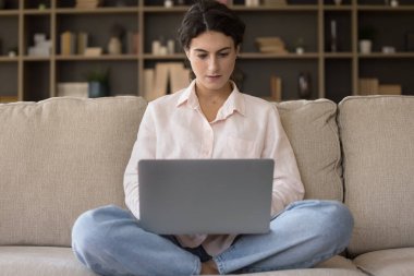 Ev koltuğunda dizüstü bilgisayar kullanan, internetten ders çalışan, Webinar izleyen, öğretmenler konferansı veren, sanal sınıfa odaklanmış Latin öğrenci kız. Oturma odasındaki bilgisayar projesinde çalışan genç serbest kadın.