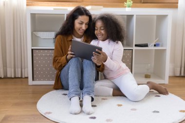 Pozitif genç anne ve mutlu Afrika jenerasyonundan Z kızı evde halılı zeminde oturuyor, elinde tablet bilgisayarla dizileri izliyor, filmleri tartışıyor, video görüşmeleri yapıyor, birlikte online kitap okuyor.