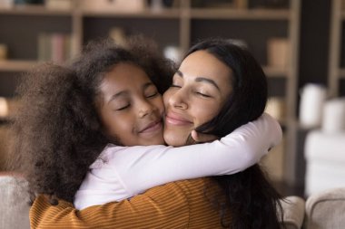 Mutlu Afrikalı anne, genç kız kızını sevgiyle kucaklıyor, şefkatle. Siyah anne ve çocuk evde kapalı gözlerle sarılıyorlar. Annelik, çocukluk, aile, anne çocuk bağlama kavramı