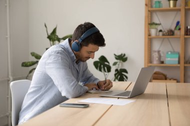 Kulaklıklı genç bir öğrenci sanal sınıfı izliyor, internette web sitesi kuruyor, online öğrenim konferansı yapıyor, evde çalışıyor, notlar yazıyor, sesli dersler dinliyor. Eğitim kavramı