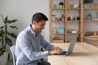 Ev işyerindeki dizüstü bilgisayarda çalışan, gülümseyen mutlu bir milenyum çalışanı. İşletme profesyoneli müşteriyle konuşuyor, online uygulama kullanıyor, internete danışıyor, video görüşmesi yapıyor.