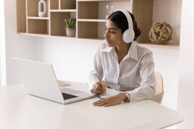 İnternet üzerinden iş konferansına katılan Hintli genç bir kadın video dersine girip notlar yazıyor uzaktan bilgi alıyor. Uzman danışman kulaklıkta pc uygulaması üzerinden uzak mesafede yardımcı istemci