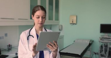 Beyaz önlüklü genç teşhis sonografisi çalışanı dijital tablet ultrason muayenesi kullanarak iş yerinde duruyor ve modern uygulama aracılığıyla hastalara uzaktan eğitim veriyor.