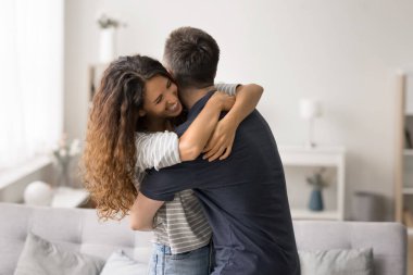 Neşeli, güzel Latin bir eş kocasını sevgiyle, sevgiyle, minnettarlıkla, neşeyle kucaklıyor. Mutlu genç çift evde tutkuyla sarılıyor, oturma odasında dans ediyor, hareketten hoşlanıyor, yakınlıktan hoşlanıyor.
