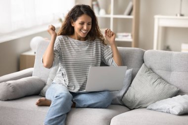 Neşeli genç serbest çalışan kadın online iş başarısını kutluyor, dizüstü bilgisayarda kazanıyor, el ele tutuşuyor, gülümsüyor, gülüyor, mutlu oluyor, heyecanlanıyor, internet bağlantısı teknolojisinden keyif alıyor.