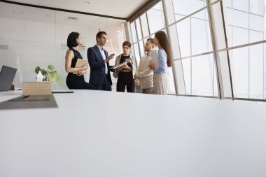 Ofis masası masası yüzeyi çeşitli iş ekiplerinin dikilip arka planda konuştuğu bir yer. Çok ırklı meslektaşlar işbirliği odasında takım çalışmasını tartışıyor