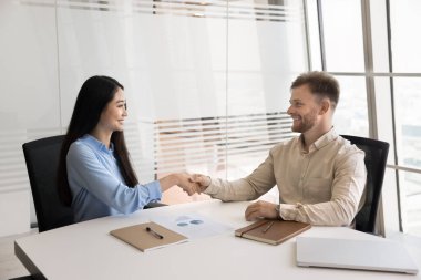 Mutlu çok ırklı girişimciler ofiste el sıkışıyor, masada konuşuyor, takım çalışmasını, ortaklığı tartışıyor. Genç Asyalı kadın iş adamı ortağına tokalaşıyor