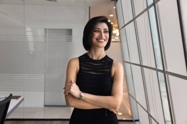 Mutlu, kendinden emin, genç proje yöneticisi iş başarısının tadını çıkarıyor, ellerini çapraz tutuyor, pencereye bakıyor, gülümsüyor, gülüyor, mesleki kariyer büyümesini düşünüyor.