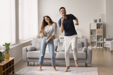 Neşeli, aktif, genç bir çift, boş zamanlarında eğleniyorlar, evde eğleniyorlar, geniş oturma odasında disko dansı yapıyorlar, gülümsüyorlar, gülüyorlar, yıldönümlerini kutluyorlar.