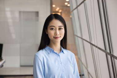 Resmî gömlekli, gülümseyen, modern ofis odasının penceresinde duran güzel, Asyalı profesyonel bir kadın. Kadın iş adamı, şirket müdürü portresi.