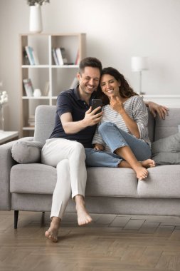 Birbirini seven romantik bir çift internet iletişimi için akıllı telefon kullanıyor rahat bir evde fotoğraf çekiyor, kanepede dinleniyor, keyfine bakıyor. Dikey çekim