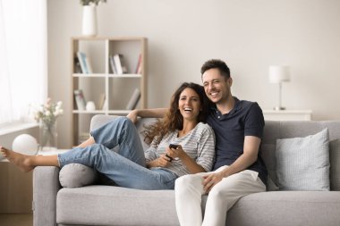 Eğlenceli, güzel çift TV 'de boş vakitlerini geçiriyor, uzaktan kumandayı kullanıyor, rahat koltukta dinleniyor, film seyrediyor, komedi programı izliyor, çevrimiçi kanal, sarılıyor, gülüyor.