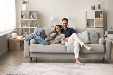 Olumlu, mutlu, genç karı ve koca rahat bir kanepede dinleniyorlar, konuşuyorlar, sarılıyorlar, gülüyorlar, eğleniyorlar, romantik eğleniyorlar, evde rahatlıyorlar, iyi sıcak ilişkiler kuruyorlar.