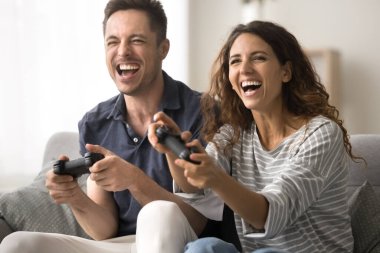 Neşeli bin yıllık karı koca evde video oyunu oynuyor, boş zamanların, sanal rekabetin tadını çıkarıyor, joysticklerin düğmelerine basıyor, gülümsüyor, gülüyor, çığlık atıyor, eğleniyor.