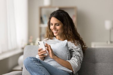 Güzel bir Latin kadının cep telefonunda uygulamayı kullanması, cihazın ekranına dokunması, gülmesi, kanepeye oturması, dijital cihazda yazması, kablosuz internet iletişiminin tadını çıkarması, sohbet etmesi.