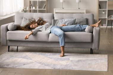 Mutlu, rahat, genç Latin kadın rahat koltukta dinleniyor, kolları açık, bacakları dağınık, uzun saçları dağınık, kameraya bakıyor, gülümsüyor, gülüyor, eğleniyor, yeni kanepenin keyfini çıkarıyor.