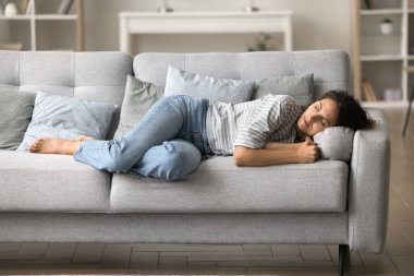 Sleepy pretty young woman resting on grey sofa at cozy home, enjoying calm leisure, relaxation, sleeping at daytime, lying on side, suffering from insomnia, sleeping disorder at night clipart