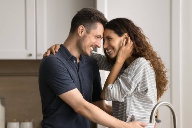 Mutlu, romantik genç çift mutfakta gülüyor, şefkatle ve tutkuyla sarılıyorlar. Koca kollarında güzel bir eş, sıcak ve sevgi dolu bir kadın.