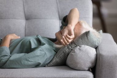 Yaşlı kadın kanepe yastığına uzanmış, yorgun, motivasyonsuz, evinde dinleniyor. Huzurlu, yaşlı bir kadın, öğle tatili yapıyor, gündüz uykusunu evde geçiriyor, stresi ve zihinsel ya da fiziksel yorgunluğu gideriyor.