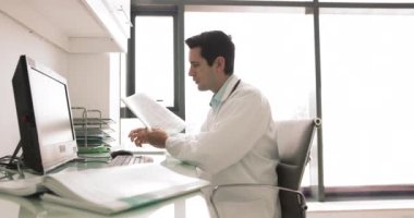 Ciddi İspanyol erkek terapist. Masasında PC ile oturuyor, araştırma yapıyor, hasta hastalıkları geçmişini inceliyor, tedavi planı üzerinde çalışıyor, hastane işyerinde evrak işleriyle uğraşıyor.