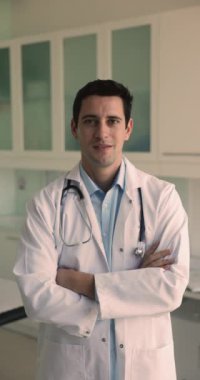 Gülümseyen, güdümlü İspanyol erkek pratisyen, özel klinik çalışanı hastanedeki muayene odasında beyaz önlük giyiyor. İş gününe hazır, meslekten ve tıbbi görevden memnun.