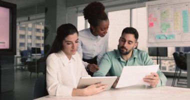 Toplantıda konuşan, ortak görevi tartışan, dijital tablet kullanan, belgelerde veri öğrenen, görüşleri paylaşan, takım çalışmasında veya ofiste brifing veren pazarlama stratejisi geliştiren üç genç çok ırklı iş arkadaşı