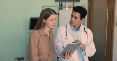 Beyaz üniformalı İspanyol erkek doktor hastayla konuşuyor, profesyonel tavsiyeler veriyor, sağlık tavsiyeleri veriyor, dijital tablette kadın ziyaretinde görüntüleri gösteren tedavi planlarını paylaşıyor.