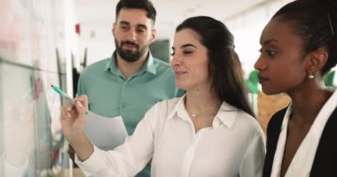 Latin kadın takım lideri beyaz tahtada sunulan bilgileri açıklıyor, çeşitli erkek takım arkadaşlarına veri sağlıyor, ortak sunum üzerinde birlikte çalışıyor, pazarlama stratejisi geliştiriyor, planlama yapıyor.
